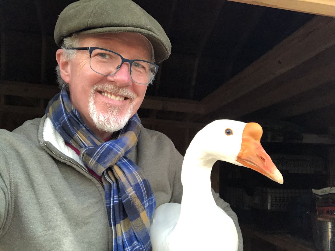 Michael Edsel smiling, with one of the geese from his mini farm